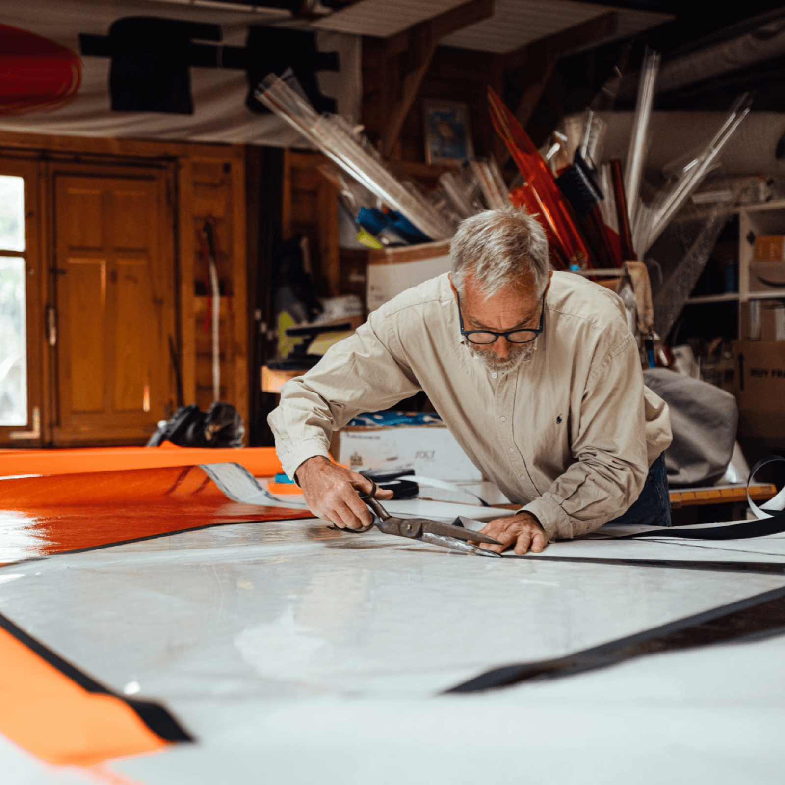 Man working on a windusrf sail in a workshop with various equipment around.