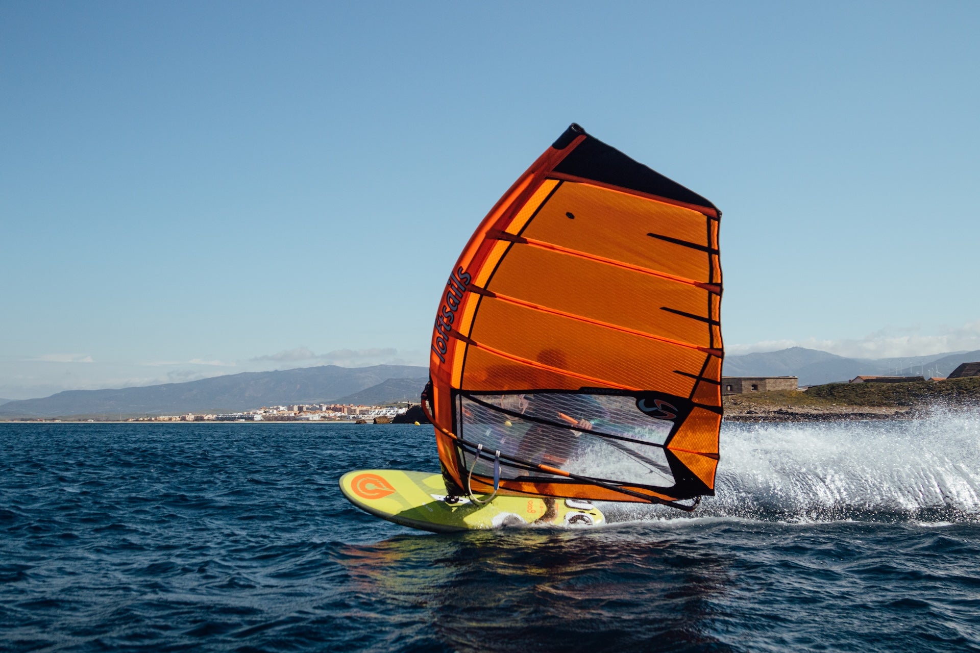 Windsurfer with an orange sail gliding over the water on a clear day.
