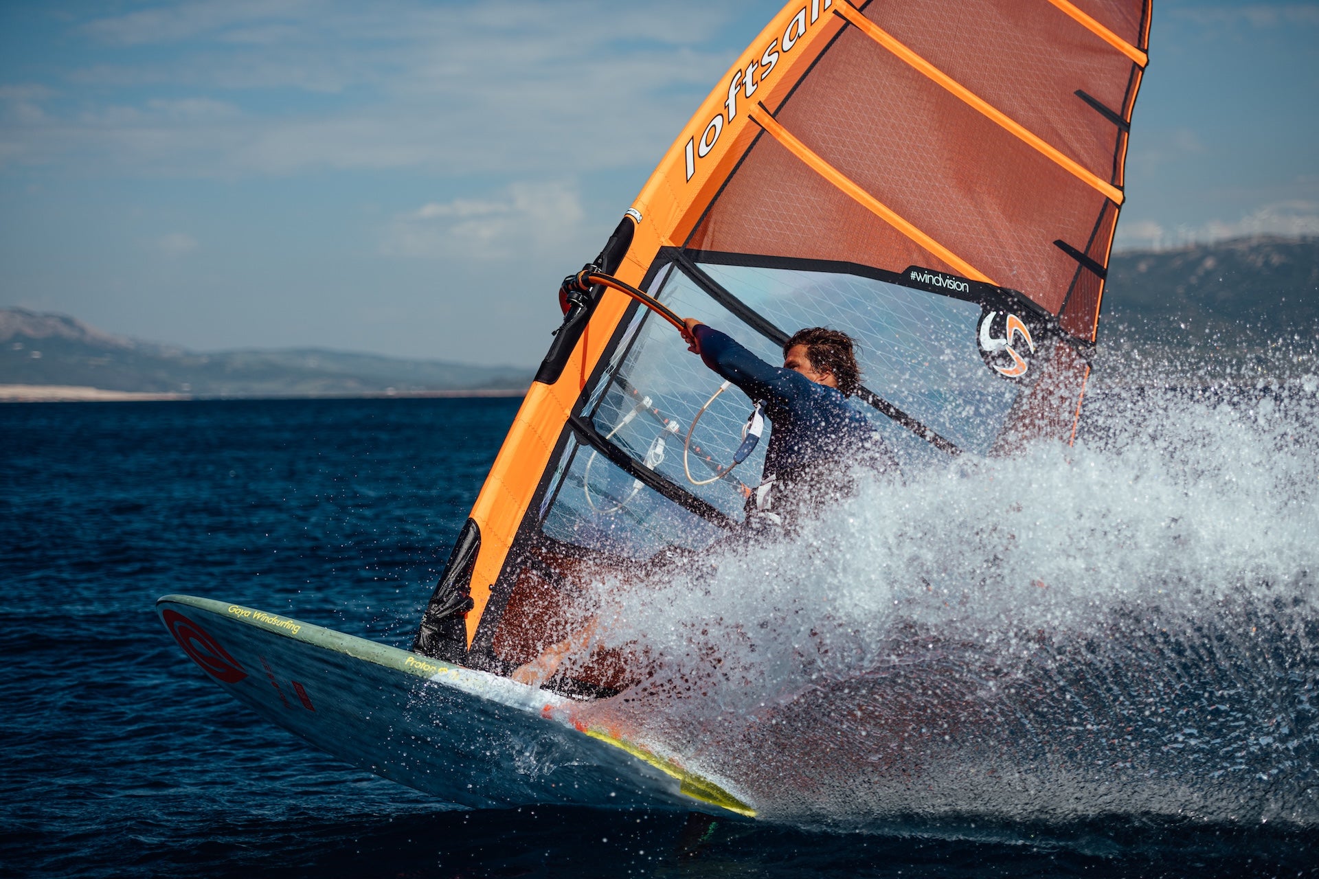 Person windsurfing on a body of water with mountains in the background