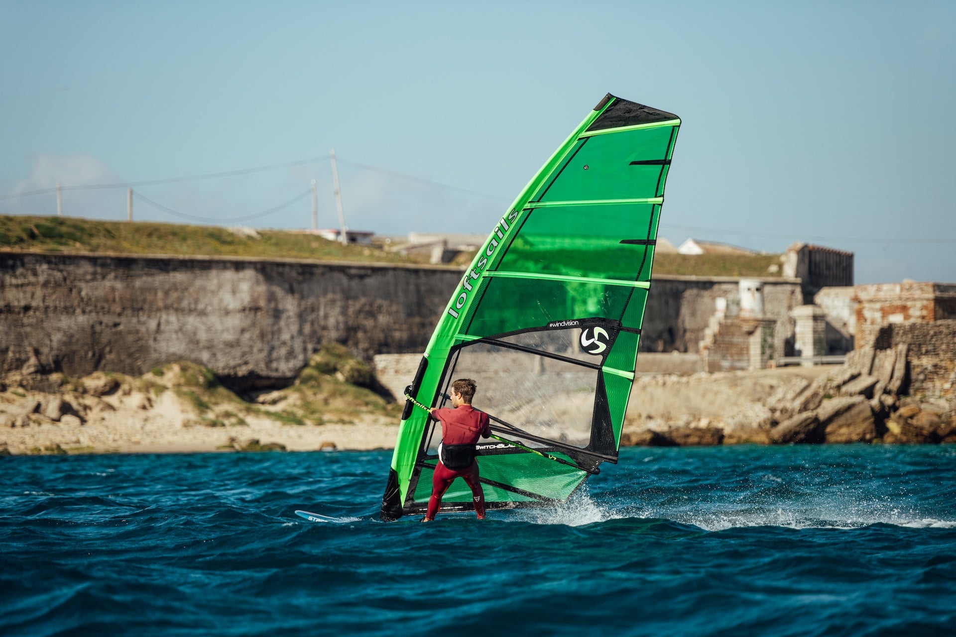 Person windsurfing on a blue sea with a coastal wall in the background