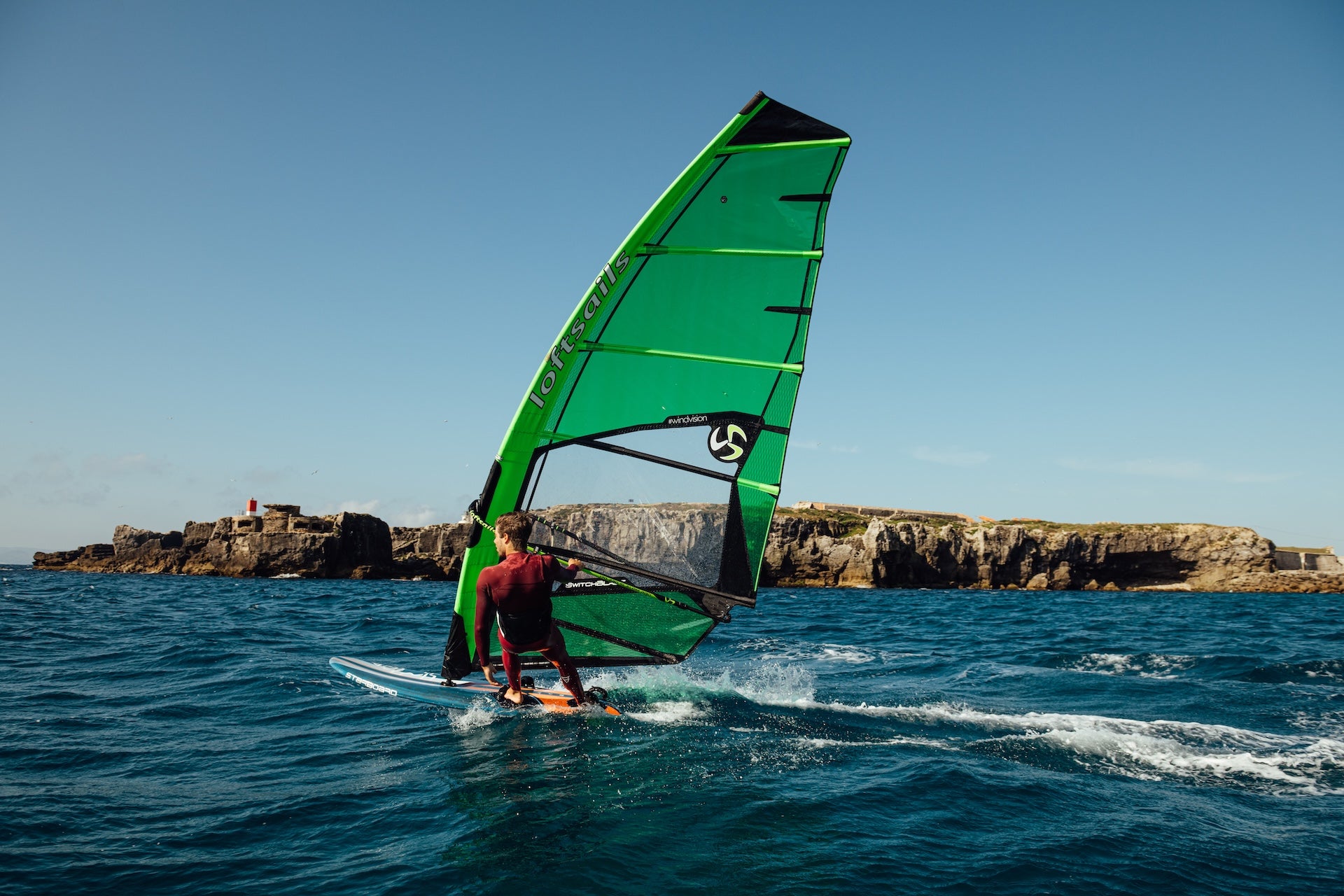 Person windsurfing on a blue ocean with rocky cliffs in the background