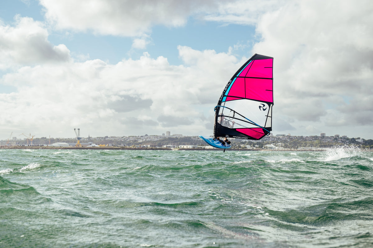 Windsurfer with a pink sail on choppy waters under a cloudy sky