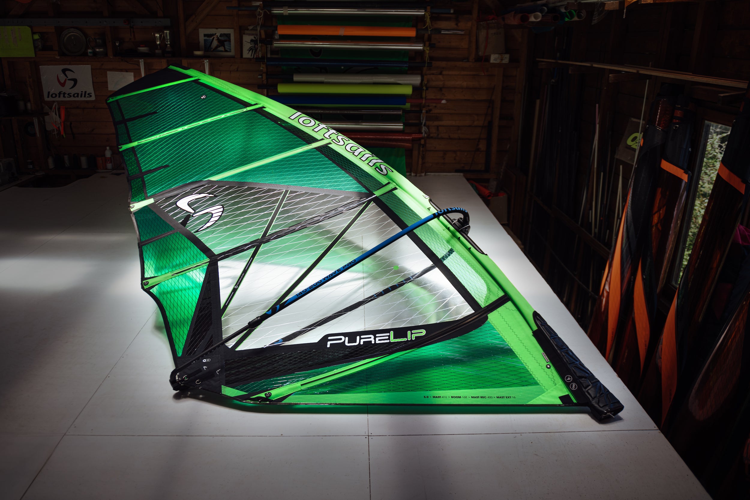 Green Loftsails Purelip 2025 windsurf sail on a table in a workshop setting
