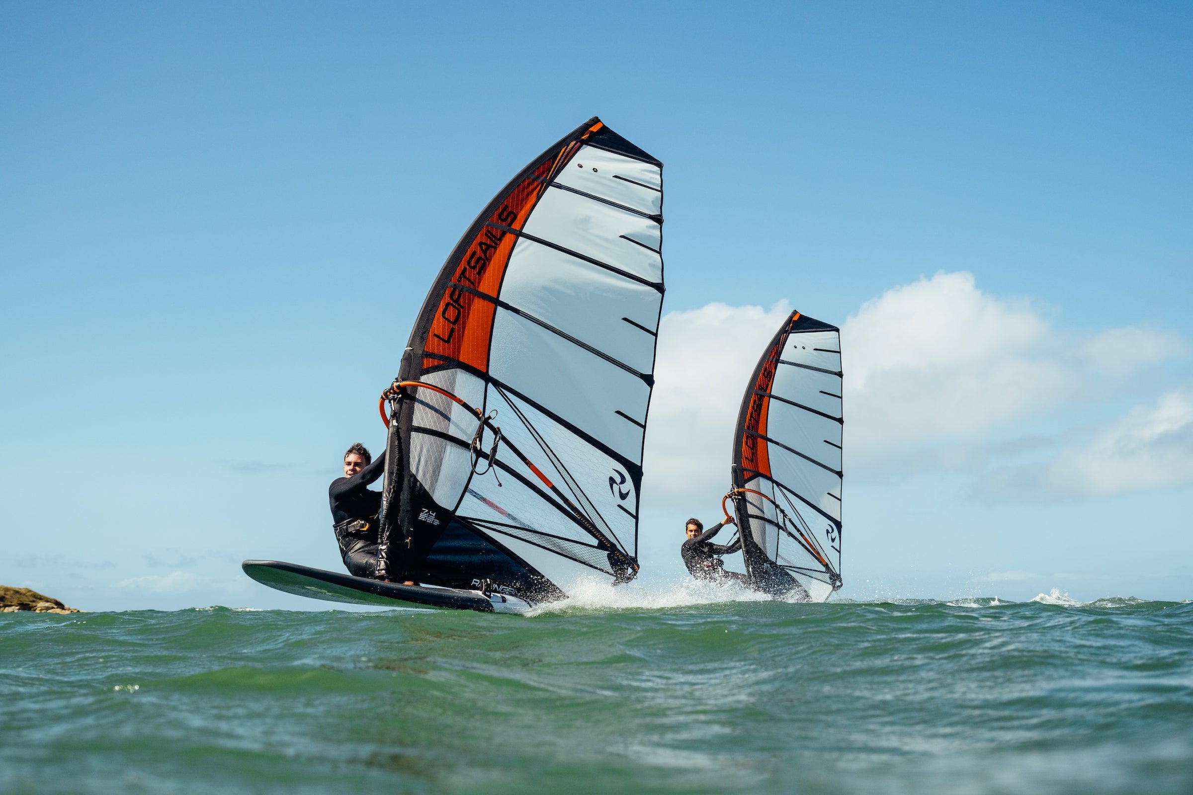 Two windsurfers on the water with clear skies